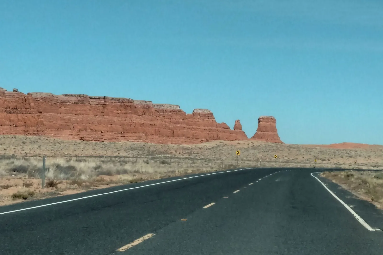 Two-lane desert road leading toward red rock hills under a clear sky