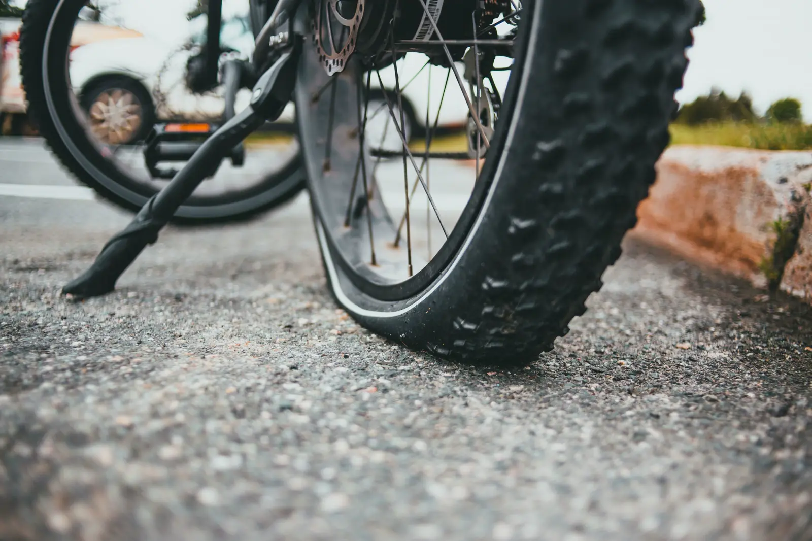 Close-up of a bicycle wheel and knobby tire on asphalt beside a concrete curb, with no people