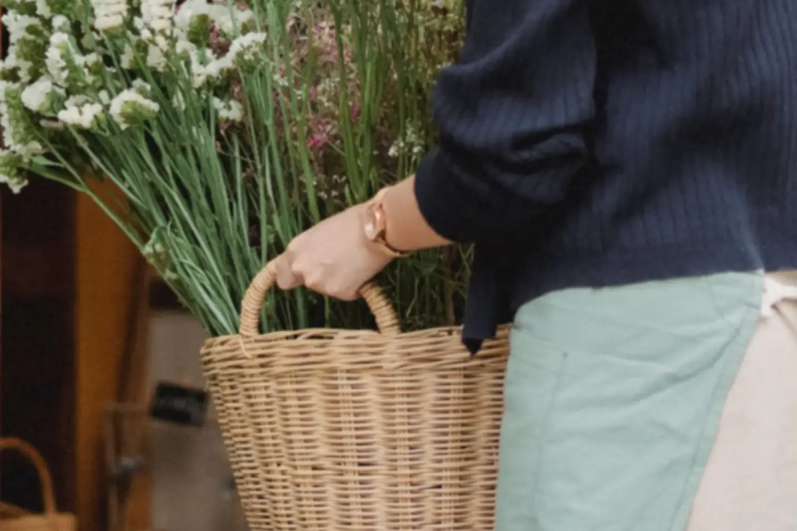 Person in an apron carrying a basket of flowers into a shop