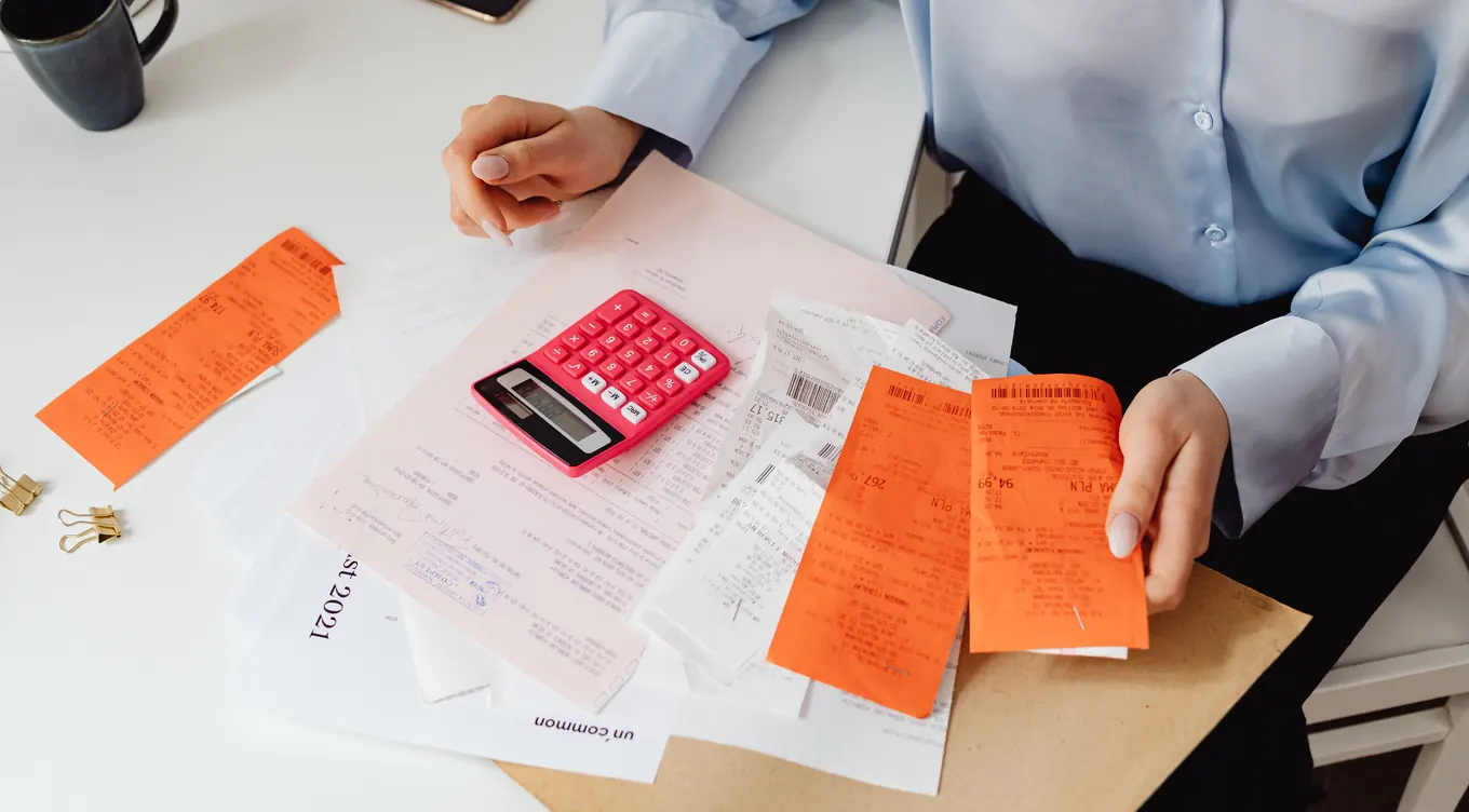 Hands sorting receipts next to a pink calculator