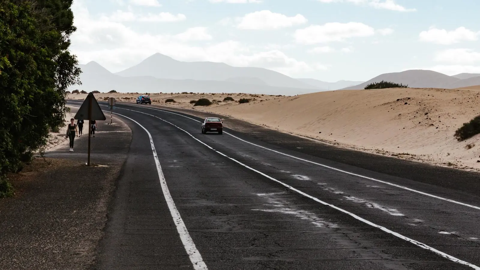 Desert highway beside sand dunes with mountains in the distance