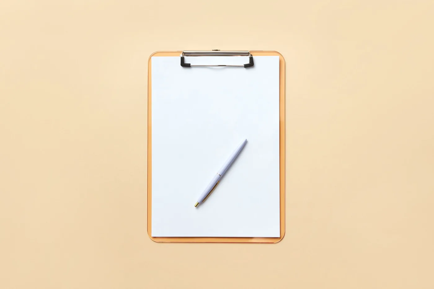 A pen and paper on a clipboard against a plain peach background