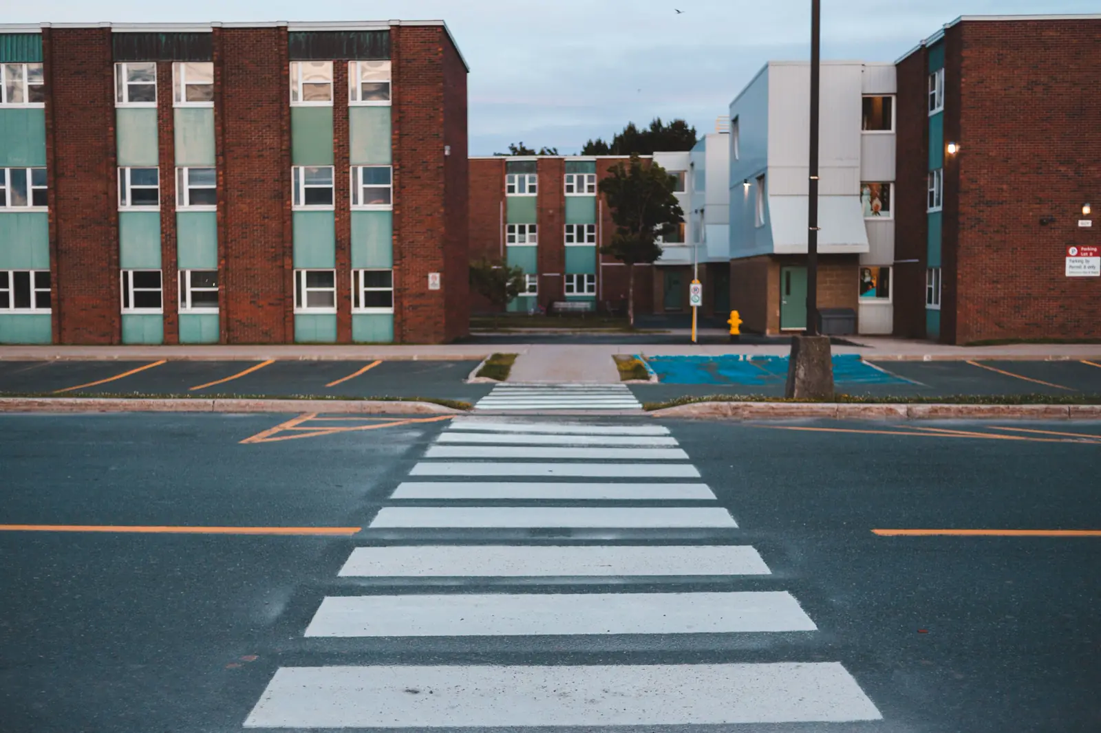 Empty striped crosswalk at dusk in front of brick apartment buildings, with no people