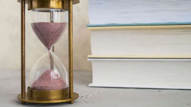 Hourglass on a desk beside a stack of papers