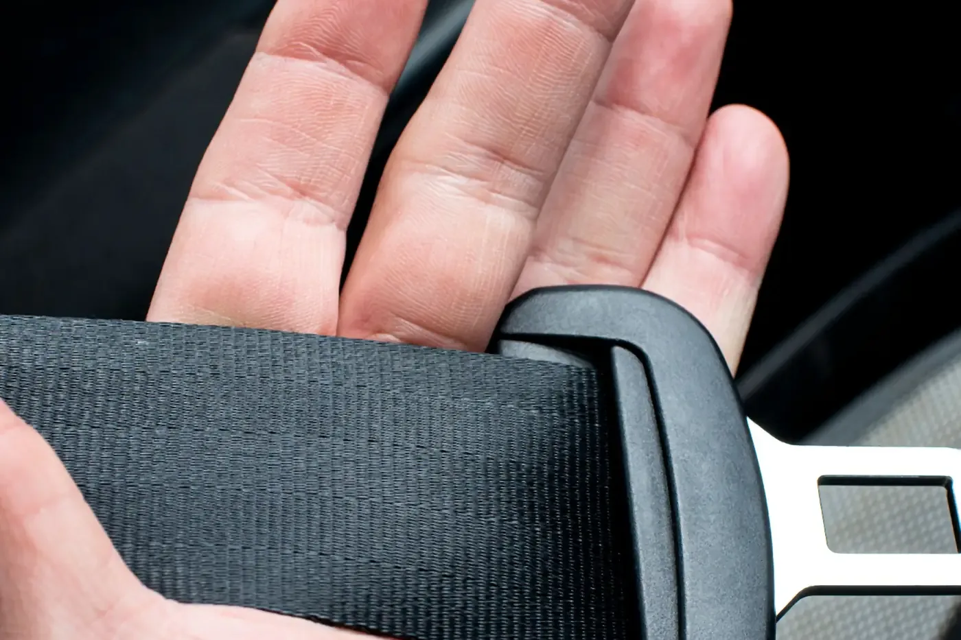 Hand holding a car seatbelt buckle inside a vehicle
