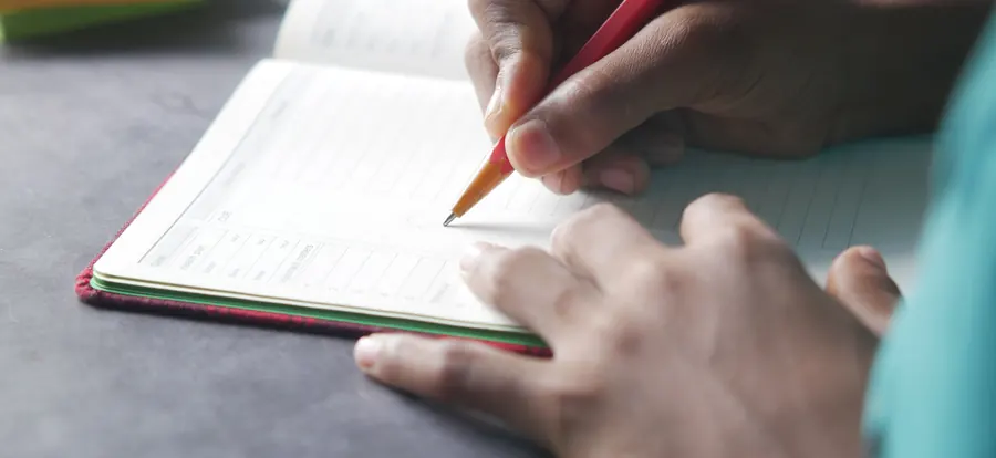 Hand writing notes with a pencil in an open notebook