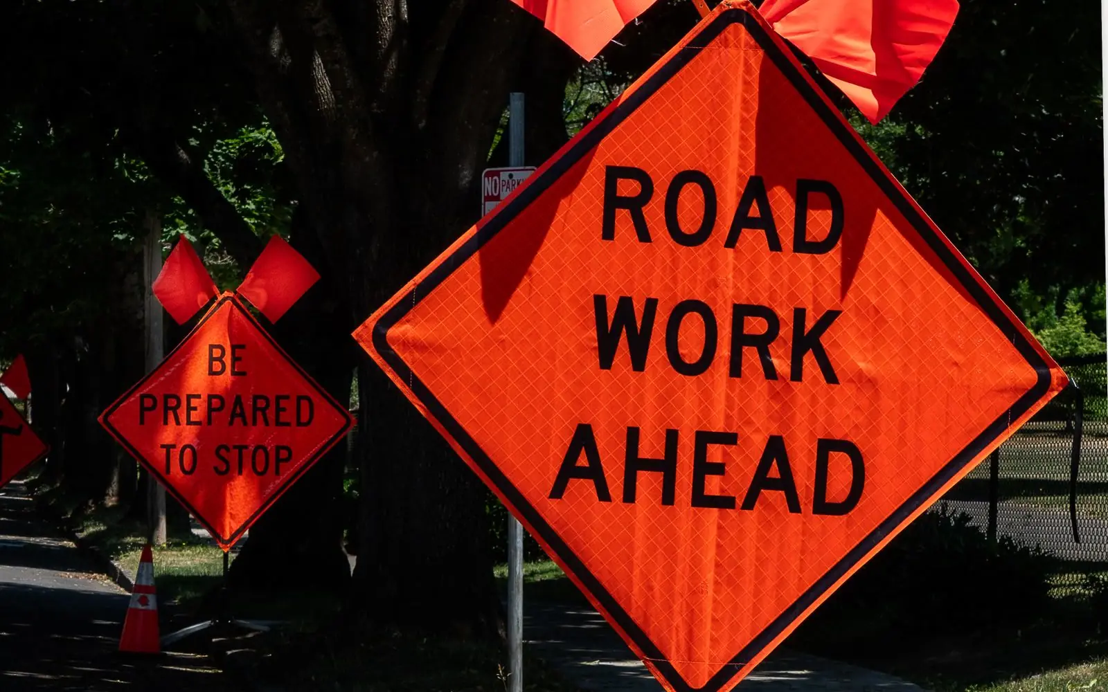 Orange road work ahead sign and traffic cone on a city street