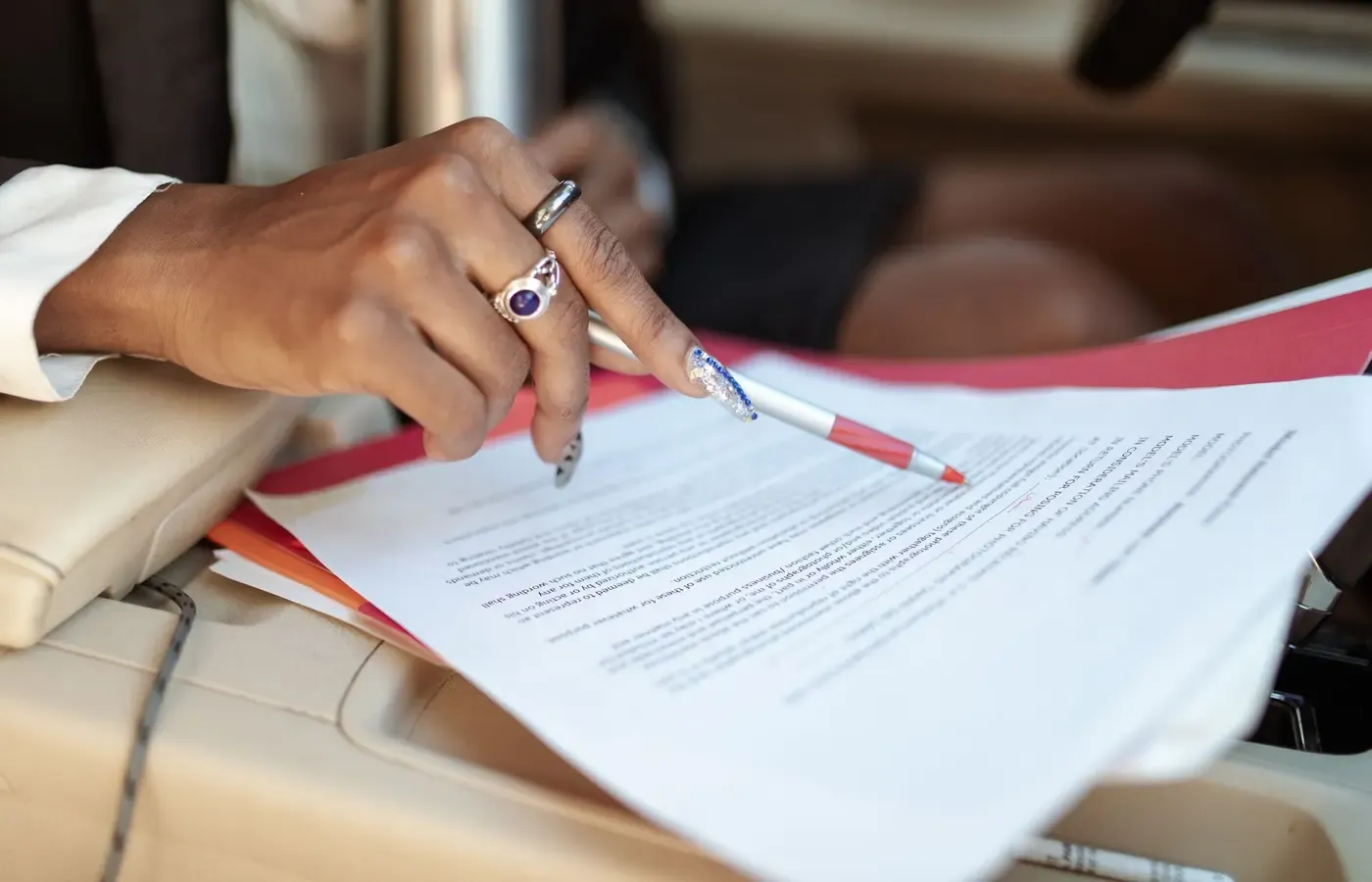 Hands holding a red pen over printed documents inside a car