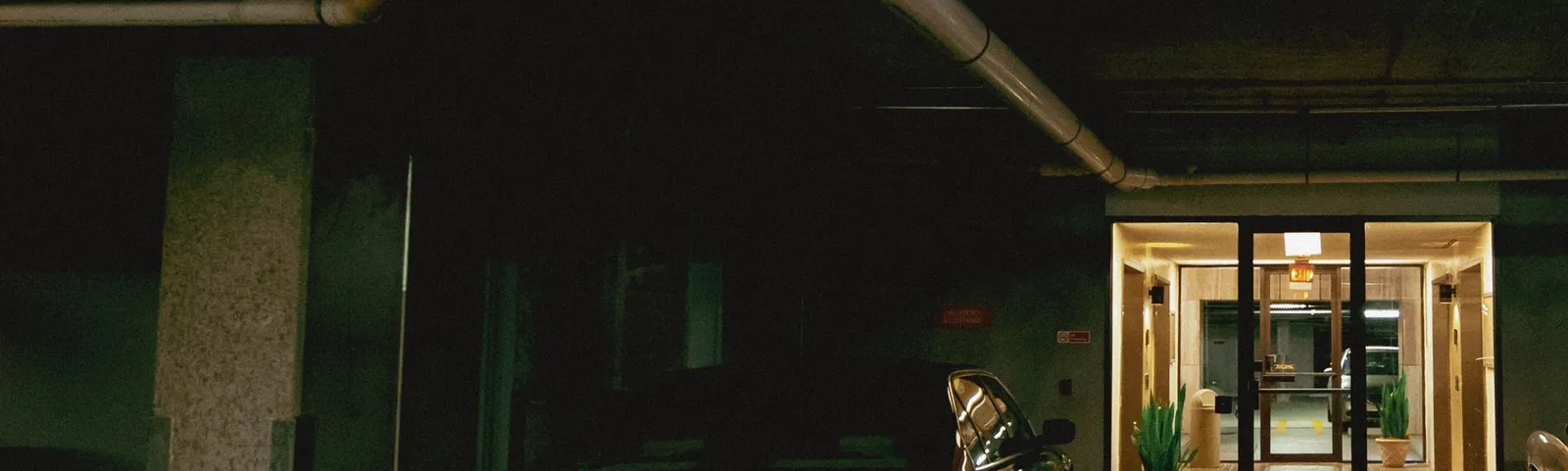 A very dark parking garage with part of a car beside a lit doorway