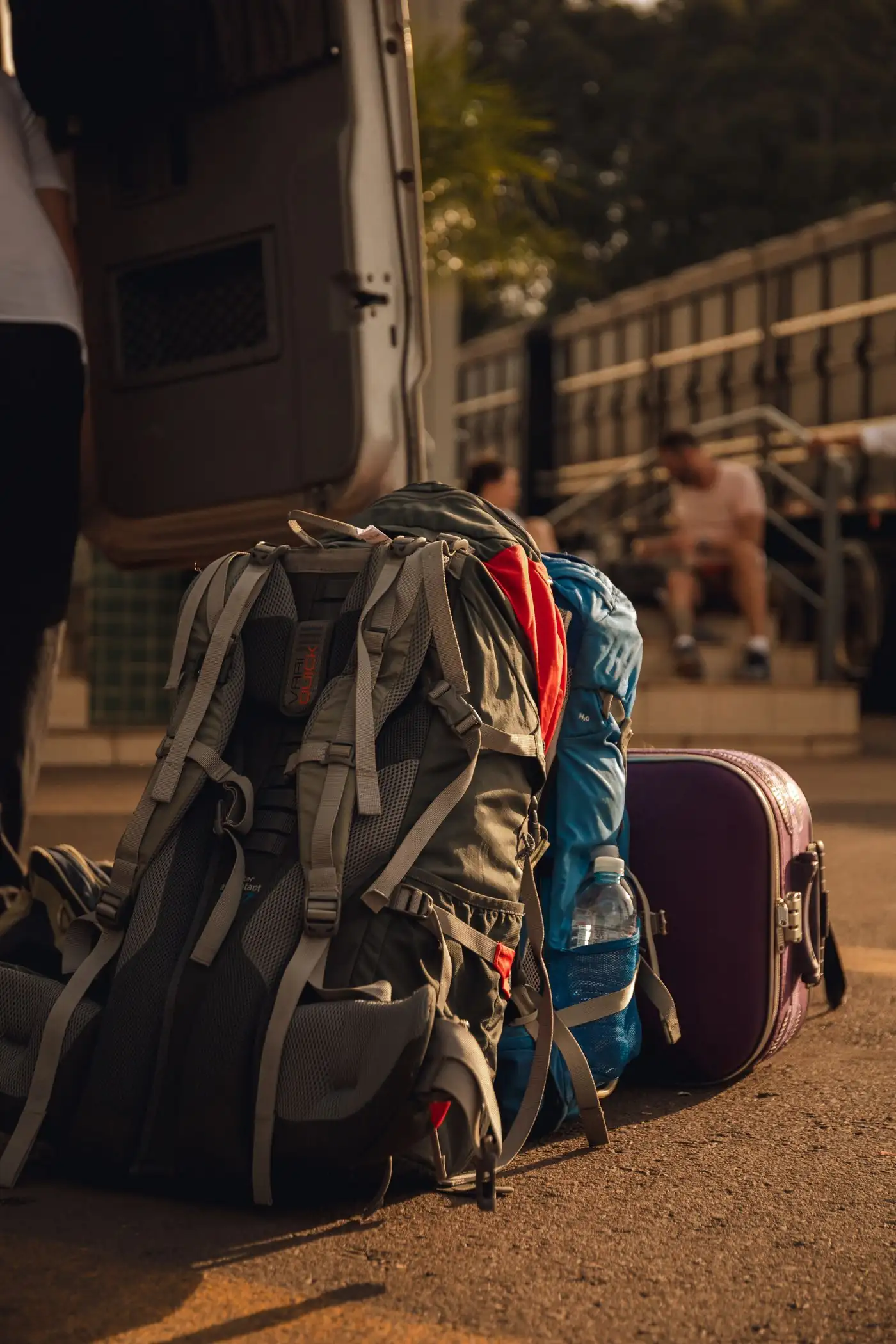 Backpacks and a suitcase on the ground next to a van